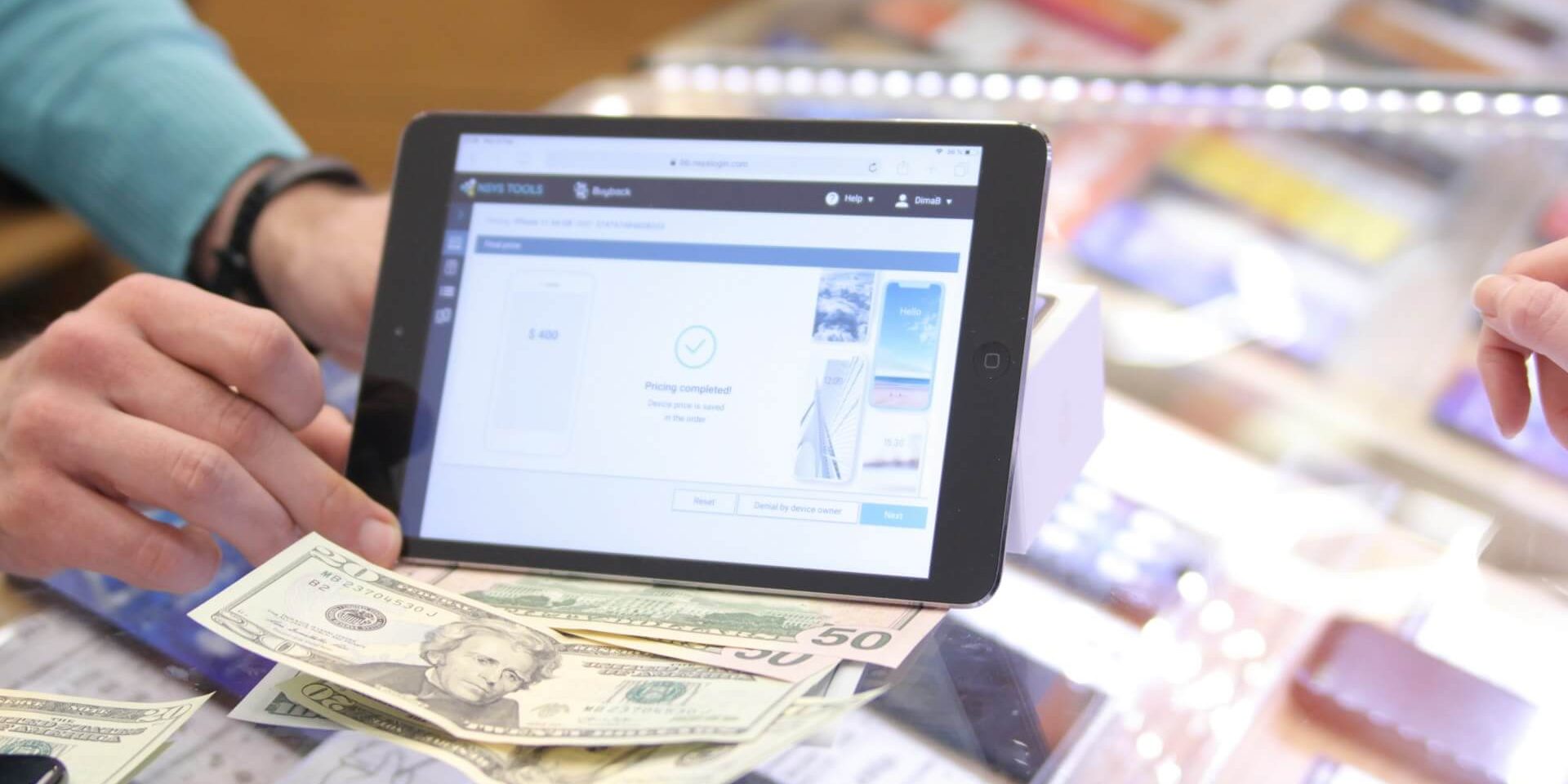 The image depicts a smartphone and accessories store, cashier holding a tablet for payment, and some cash on the counter.