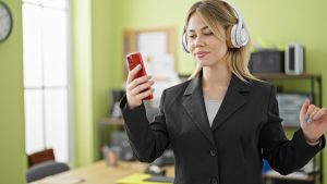 blonde girl standing in her room wearing headphones and holding her phone