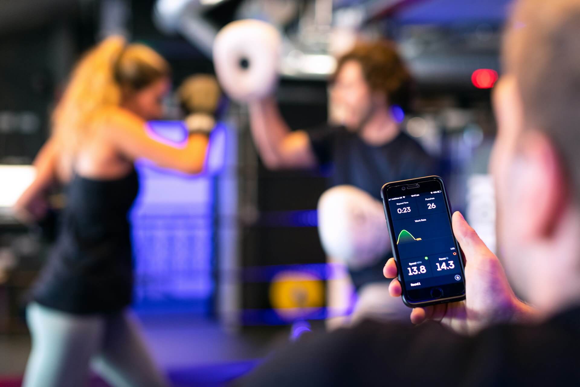 woman in gym practicing boxing, with her trainer using a smartphone to time her.