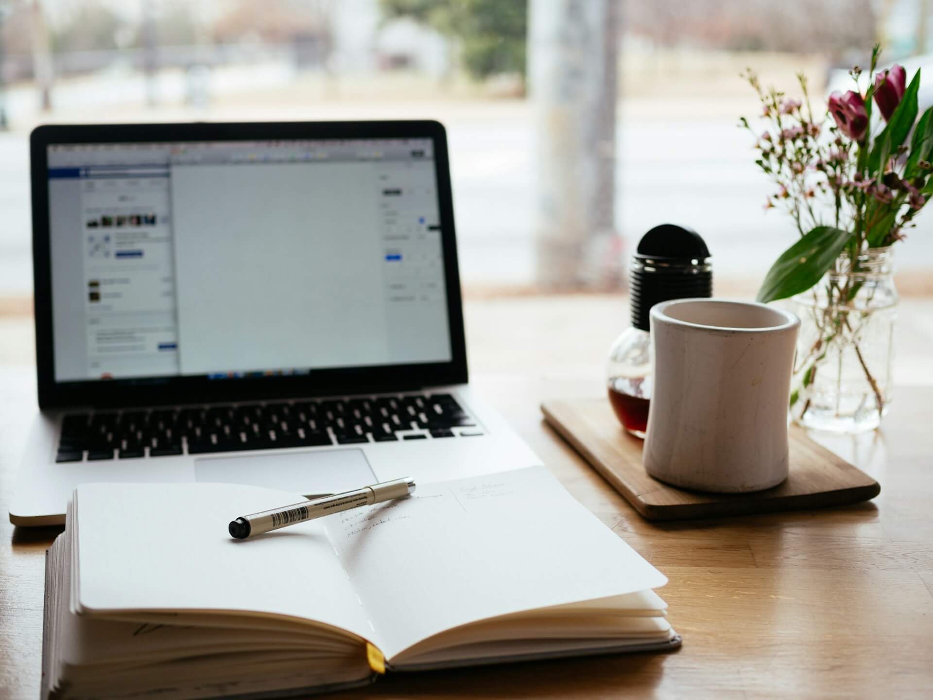 A laptop, mug, notebook and pen on a des