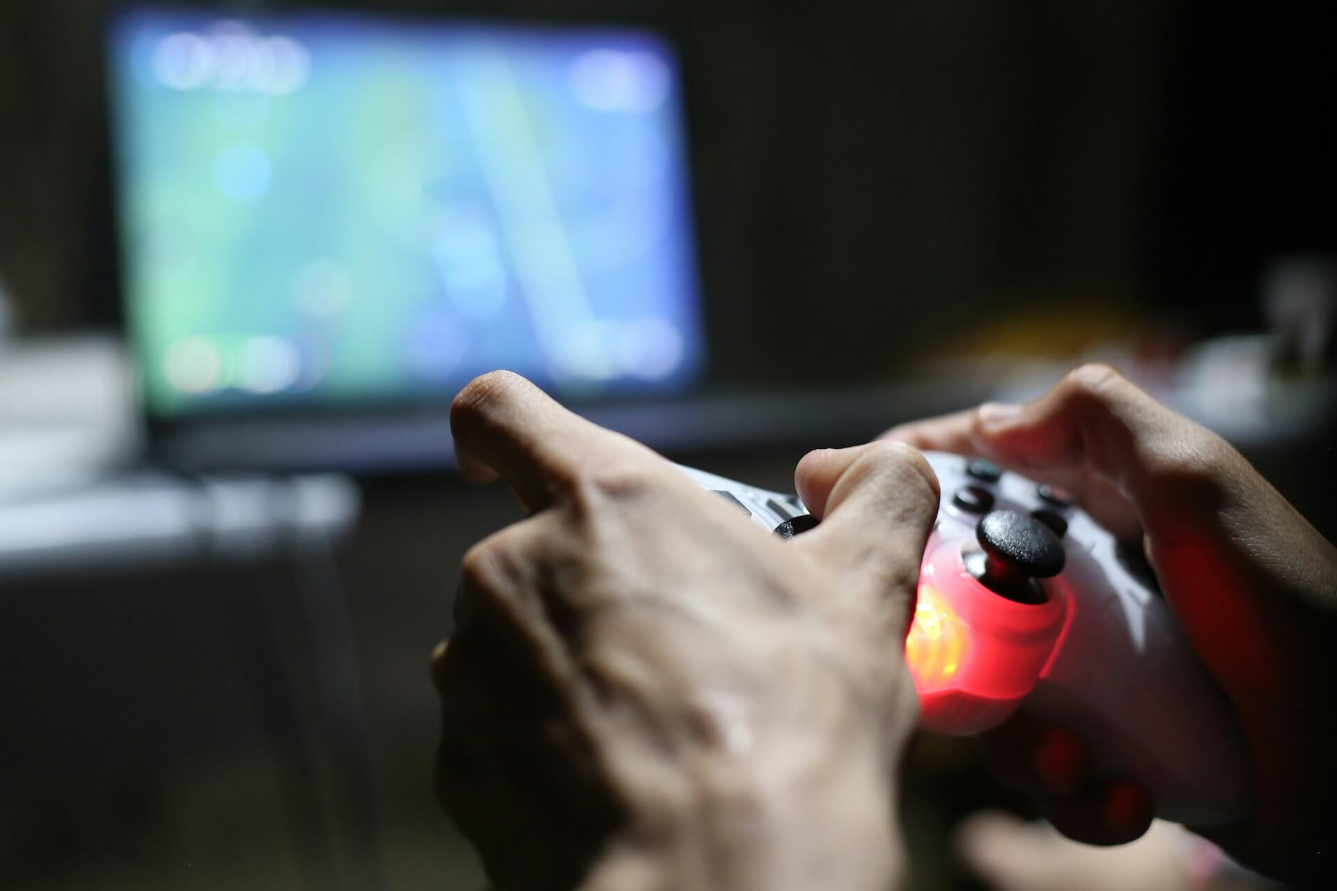 Closeup of a person' hands holding a Playstation controller, with a TV screen in front of them, blurred